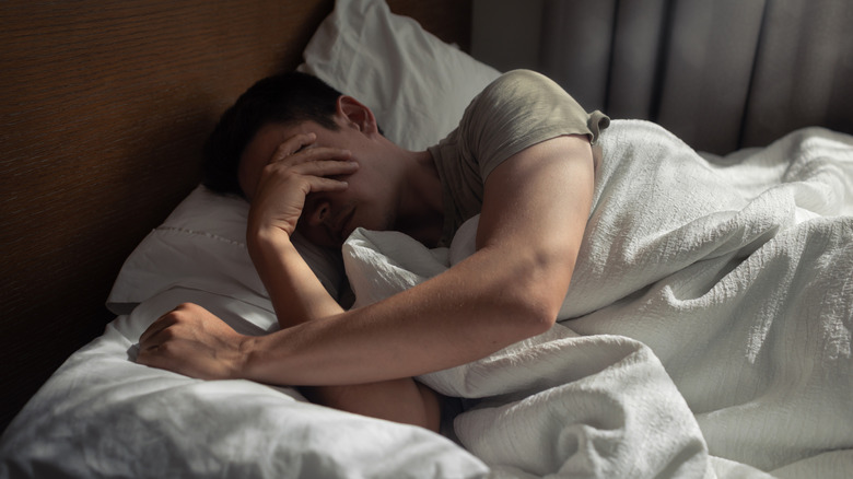 Person sleeping in bed with white sheets, pillow, and blanket during twilight hours