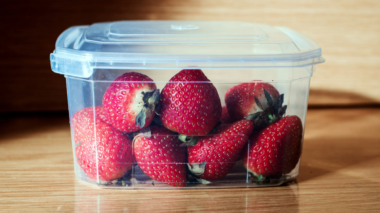 Bright red, perfectly ripe strawberries in an airtight plastic container on a wooden table