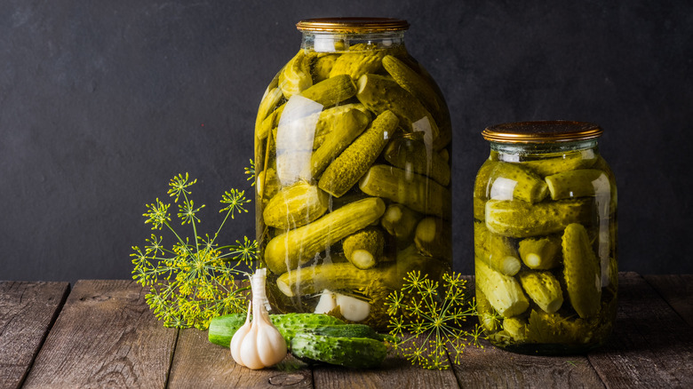 two jars of pickles surrounded by dill
