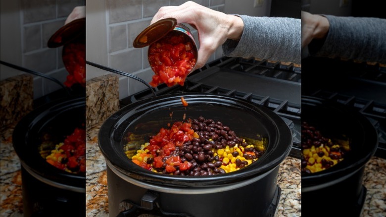 Someone adding canned tomatoes to a slow cooker of ingredients.