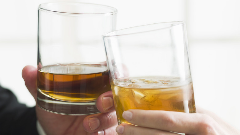 Hands holding glasses of brown liquid toasting