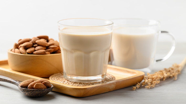 A wooden bowl of almonds next to two glasses of almond milk