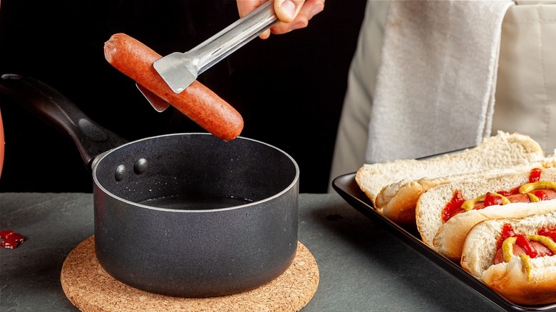 A hot dog cooked in a pot being lifted by tongs 