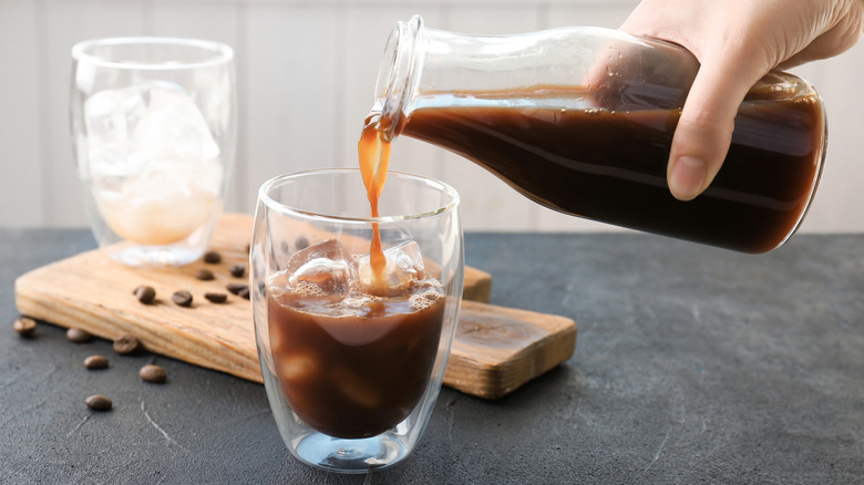 Hand pouring cold brew from bottle into glass