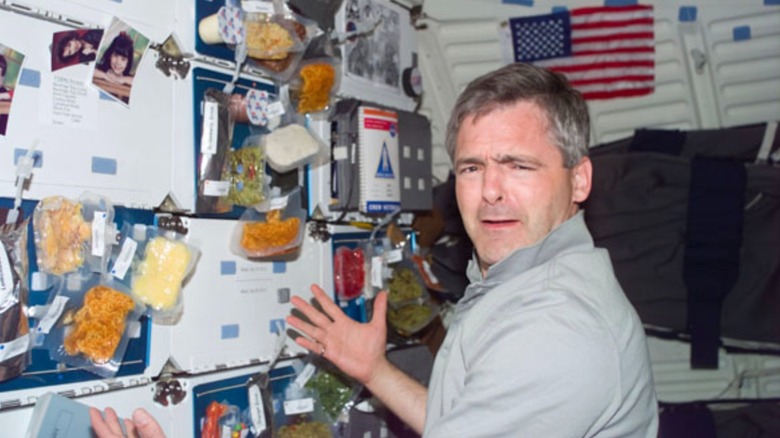 Astronaut Marc Garneau displays trays of food attached to the Endeavour's middeck lockers