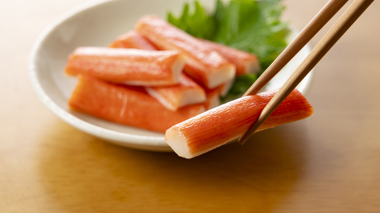 Bowl of imitation crab with lettuce and a pair of chopsticks picking up one piece