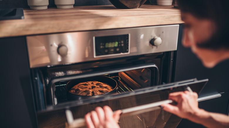 Hands opening oven door with cake baking inside