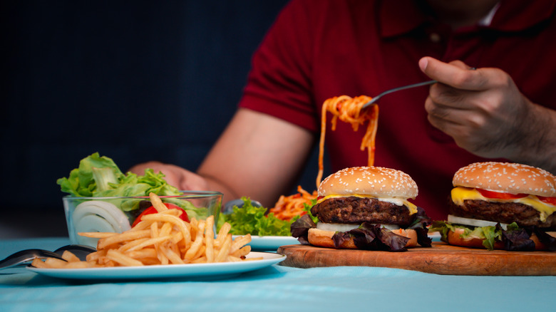 Man eating pasta, burgers, and fries