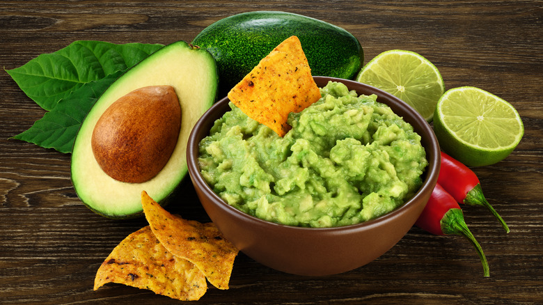 Bowl of guacamole and chips next to avocado