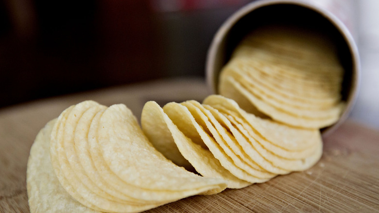 Open can of pringles with chips spilling onto table