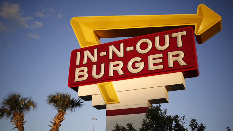 An In-N-Out road sign with palm trees and blue sky in the background