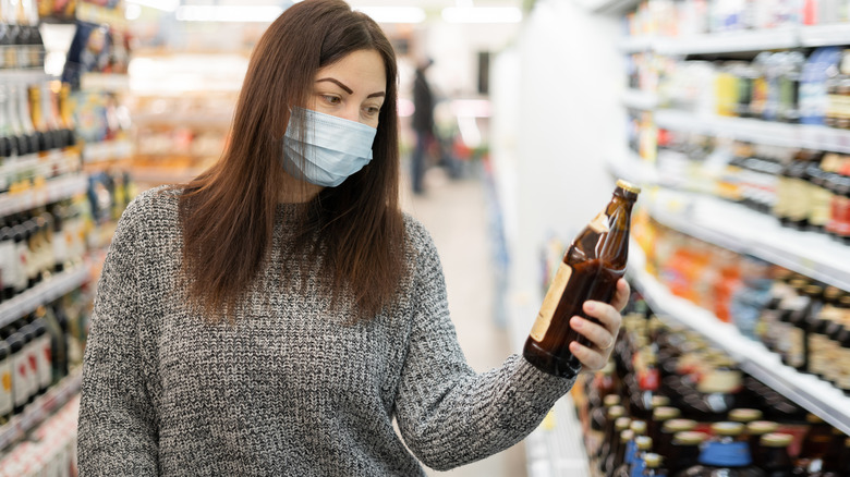 A masked woman considering a beer