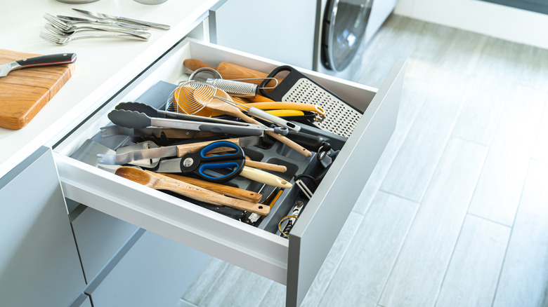 Messy kitchen drawer overflowing with utensils