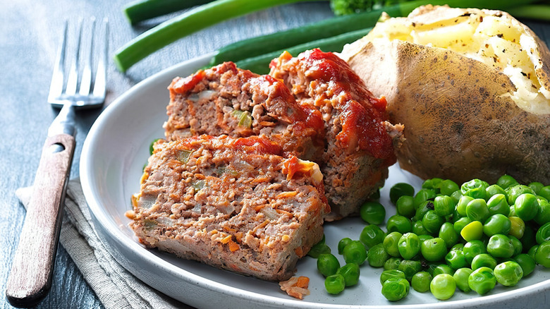Sliced meatloaf on plate with potato and peas