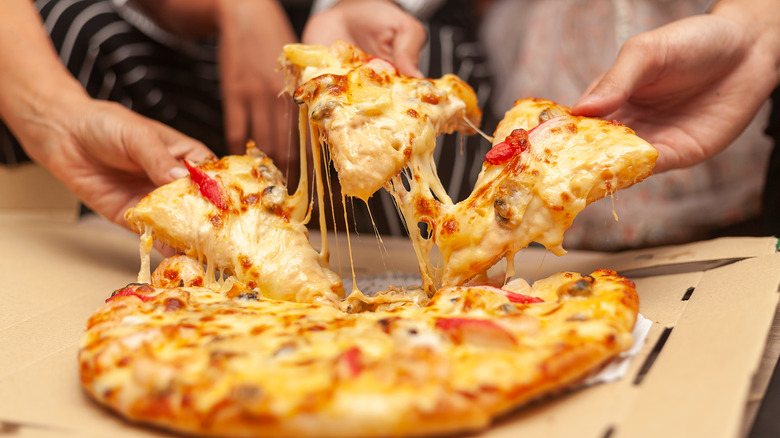 Hands grabbing slice of pizza