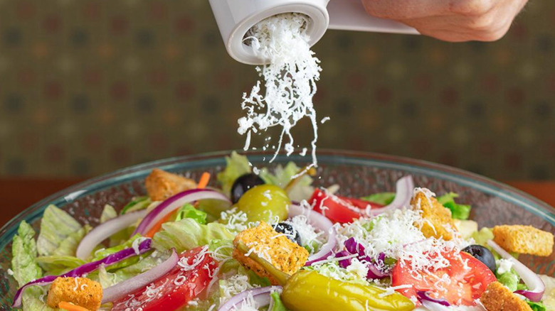 Copious cheese being hand-grated over a fresh salad at Olive Garden