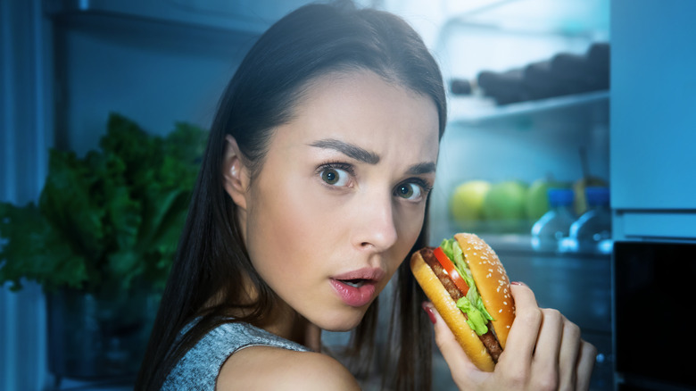 A woman eating burger at night 