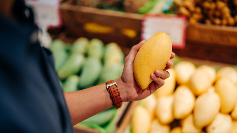 Customer's hand holding a yellow mango at a market