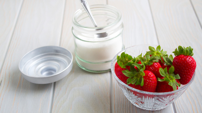 A container of sugar with the spoon inside next to a bowl of fresh strawberries.