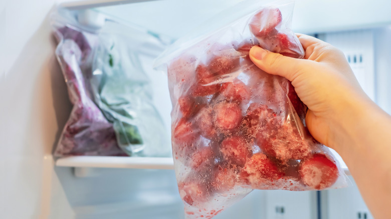 A person holding a bag of frozen strawberries in front of a freezer.