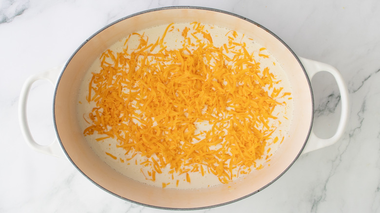 shredded orange cheese floating on white liquid in a white pot
