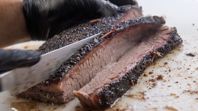 Close-up of a chef slicing juicy smoked brisket with black gloves