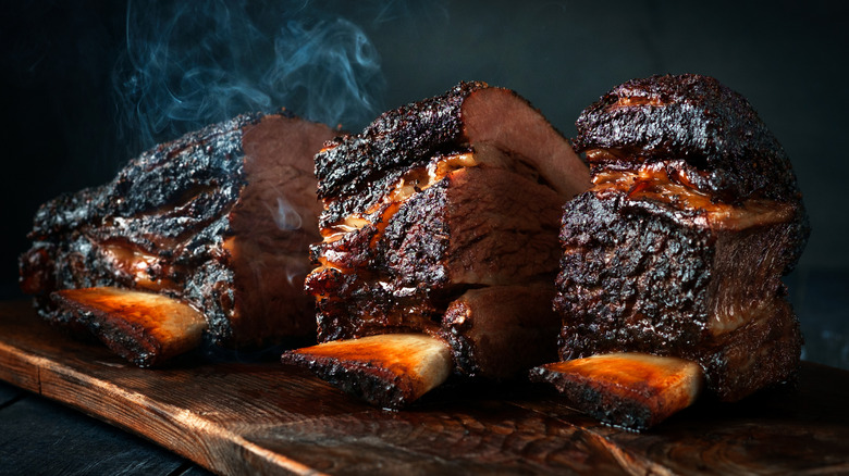 Three pieces of smoked brisket on a wooden cutting board with steam rising