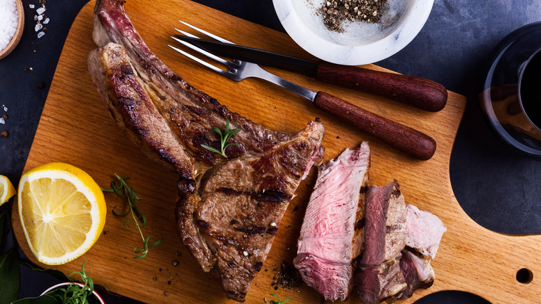 Prime rib on cutting board with fork, knife and lemon