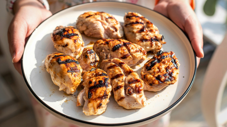 Hands holding plate of grilled chicken pieces