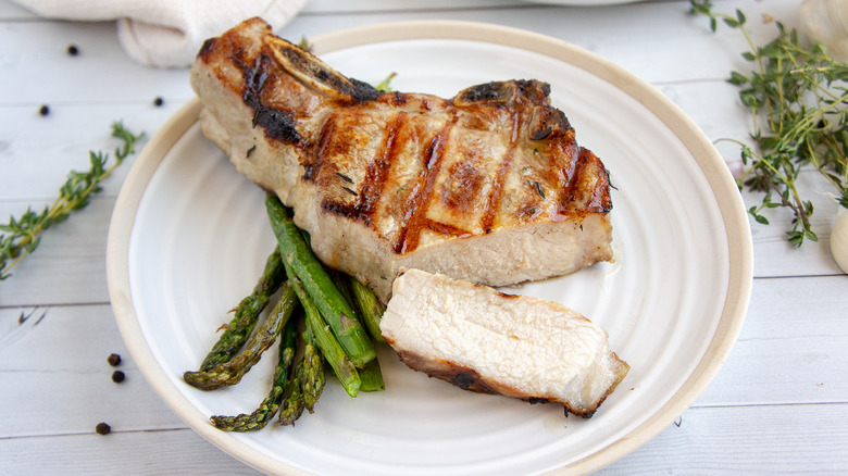 Grilled pork chop and asparagus on white plate.