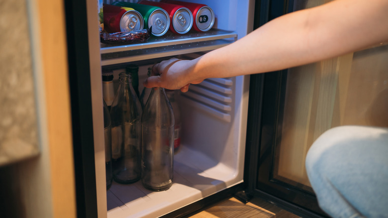 Hand grabbing a bottled beverage from the bottom shelf of a mini fridge