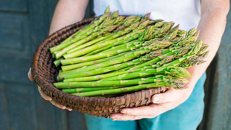 a basket of fresh asparagus is being held by someone