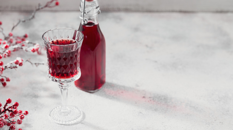 cherry infused vodka in a jar next to a glass filled with the beverage