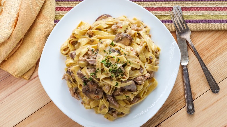 Pasta with creamy sauce and sausage on a plate with silverware