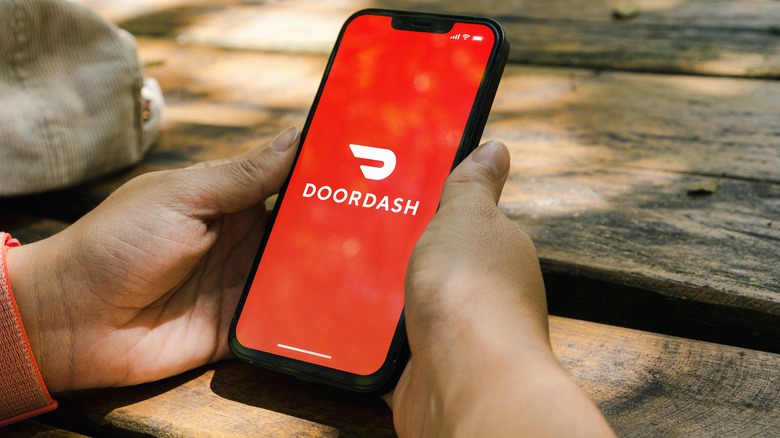 Person at picnic table holding phone with doordash logo