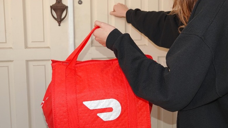 DoorDash delivery driver knocking on a door and holding a takeout bag