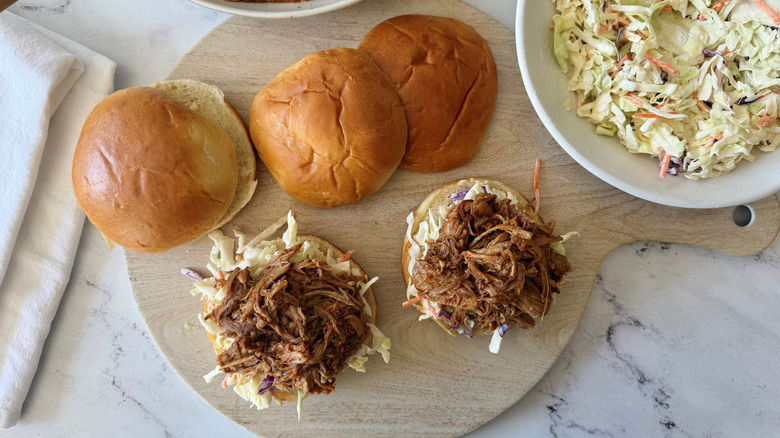 Uncapped pulled pork sandwiches next to top buns and coleslaw