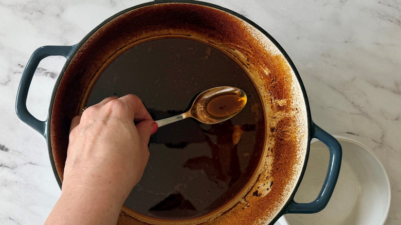 Hand using spoon to scoop liquid out of Dutch oven