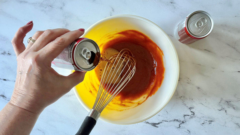 Hand pouring Dr Pepper into bowl of sauce with whisk