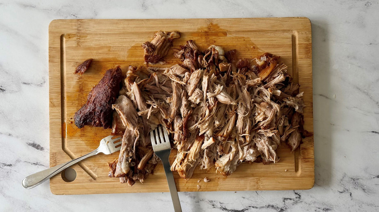 Shredded pork with forks on wooden board