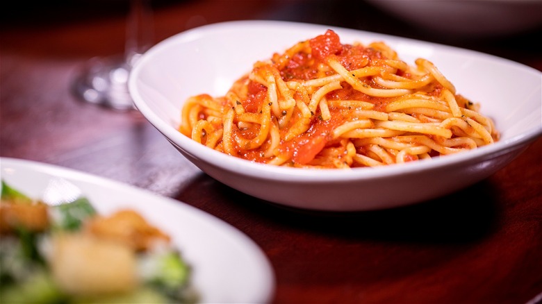 A small dish of spaghetti with a bowl of Caesar salad in the foreground