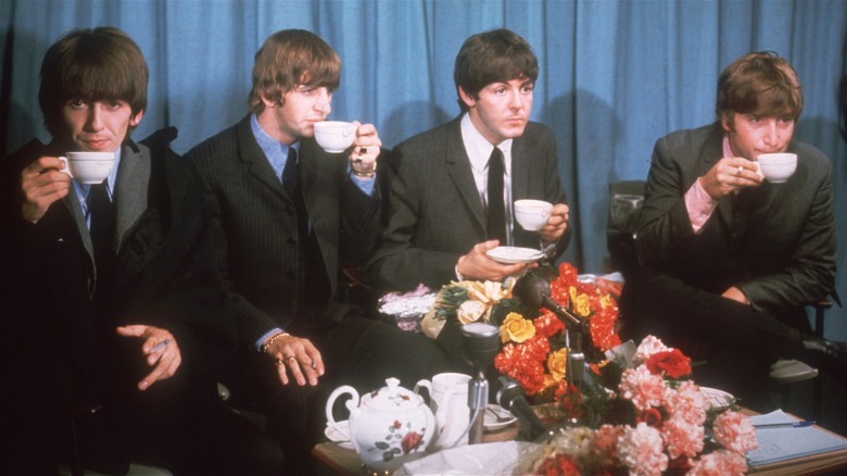 The Beatles drinking cups of tea during a press event.