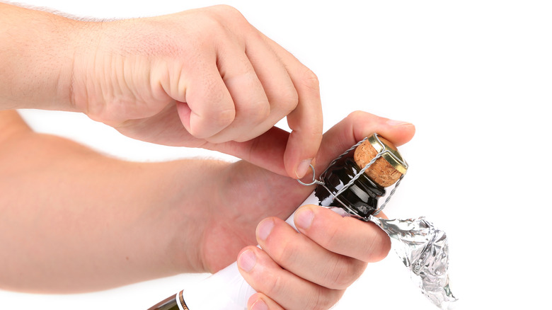 hands opening a bottle of champagne, holding the cork with the thumb and removing the cage