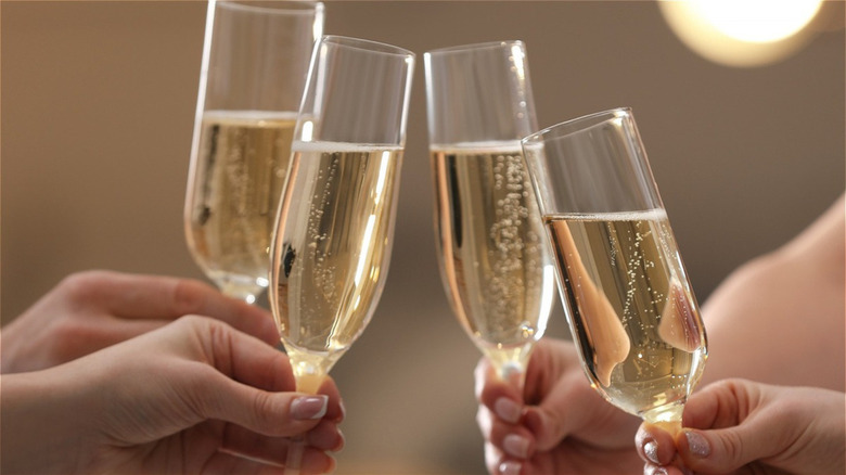 a group holding four champagne flutes about to clink glasses