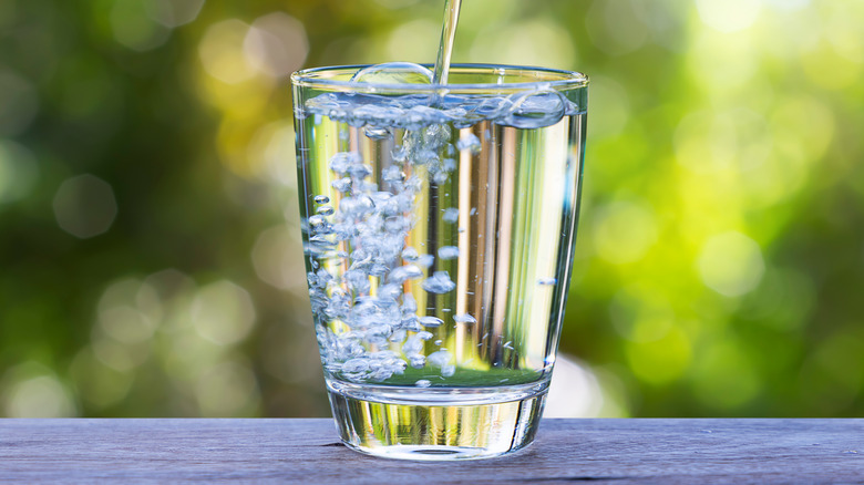 Water pouring into clear glass on table outside.