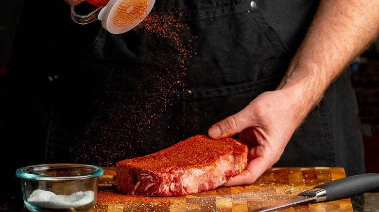 Person shaking dry rub seasoning on a steak