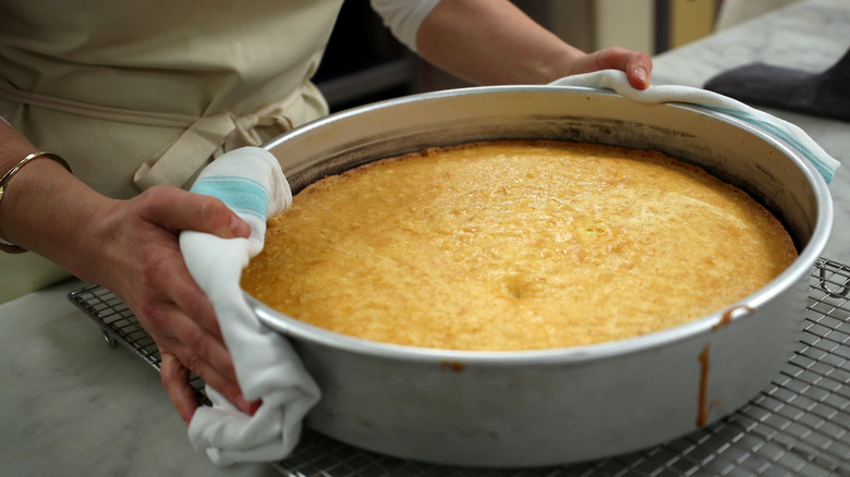 A person holding a cake in a pan.