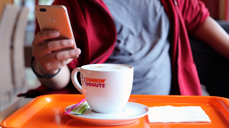 Man drinking Dunkin' coffee and looking at phone 