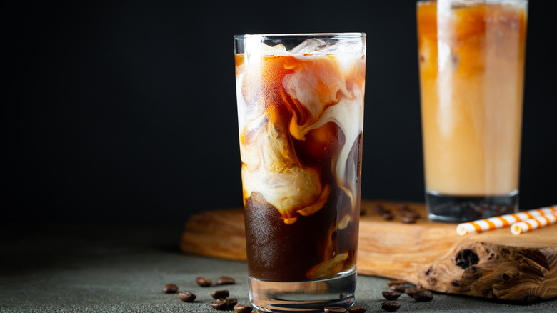 Two glasses of iced coffee with milk swirling