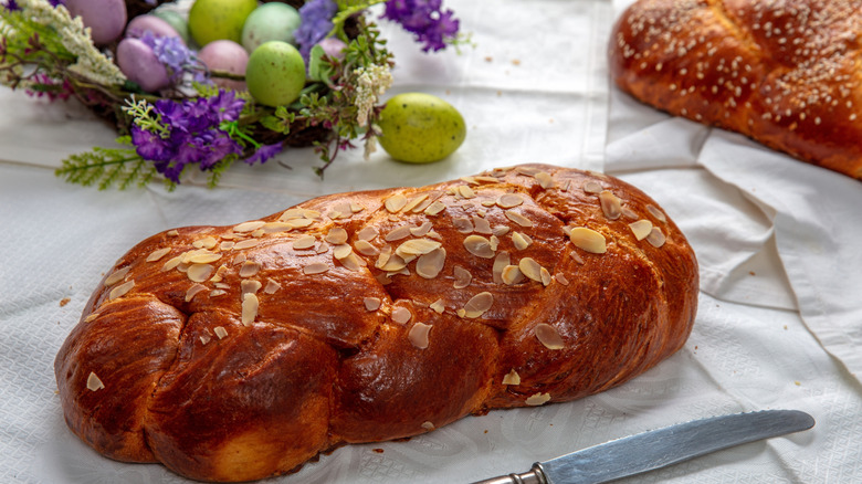 Loaves of tsoureki braided bread topped with sliced almonds, surrounded by painted eggs